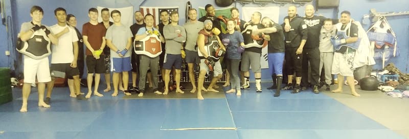 TCB members line the mat in front of a wall of championship belts.