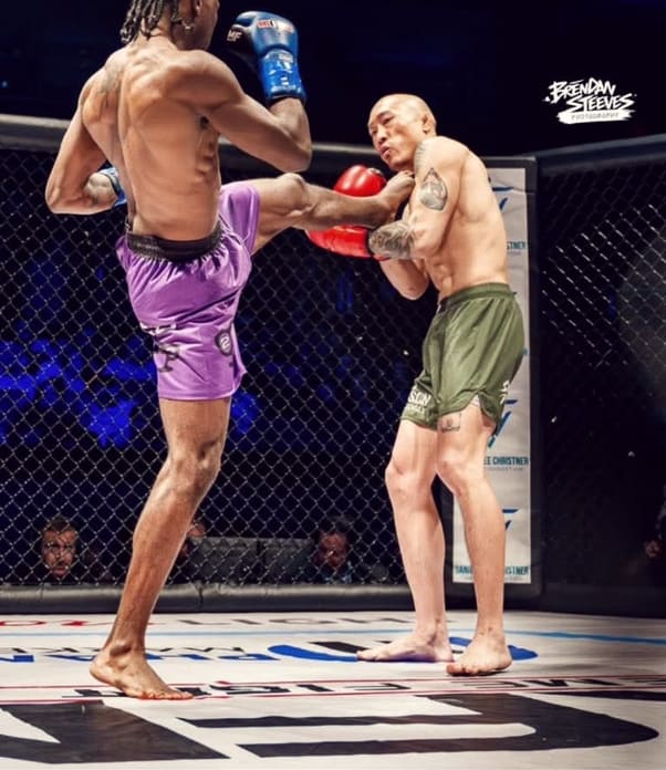 A TCB fighter in purple shorts throws a body kick in the cage.