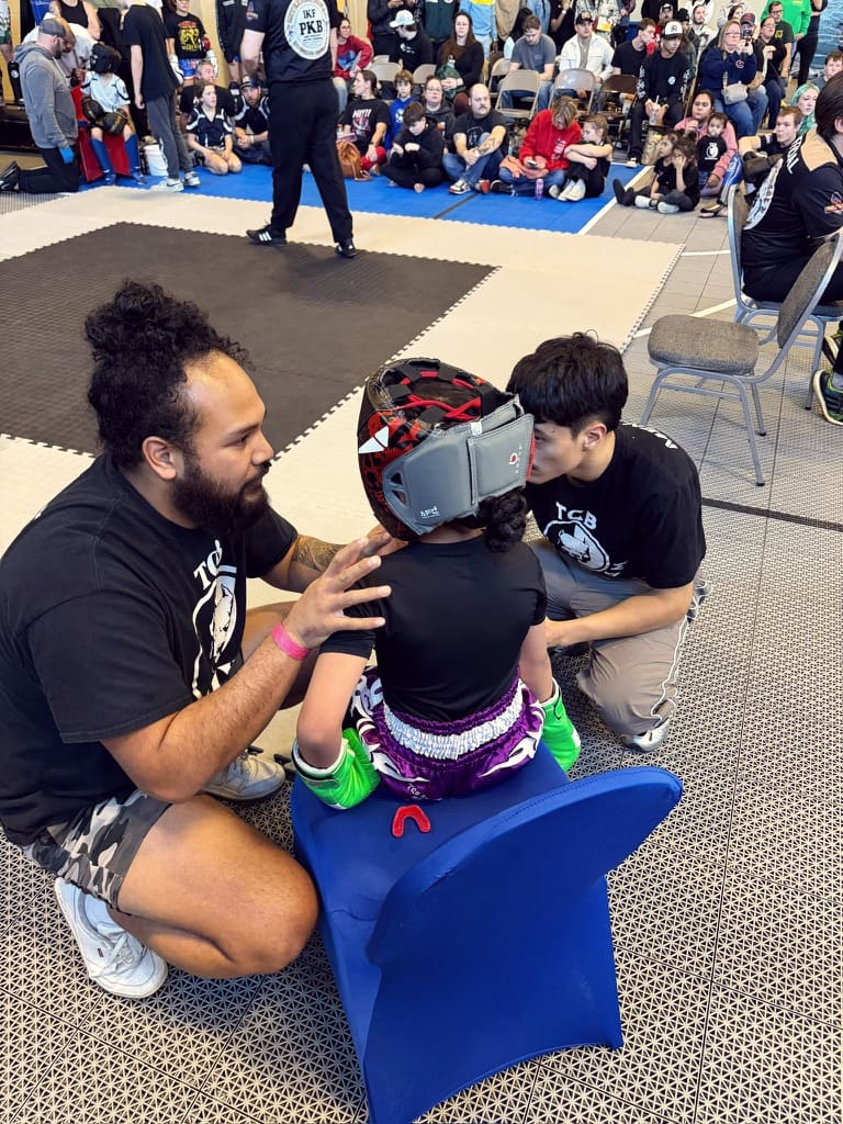 A TCB coach fits headgear on a young fighter between matches at a tournament.