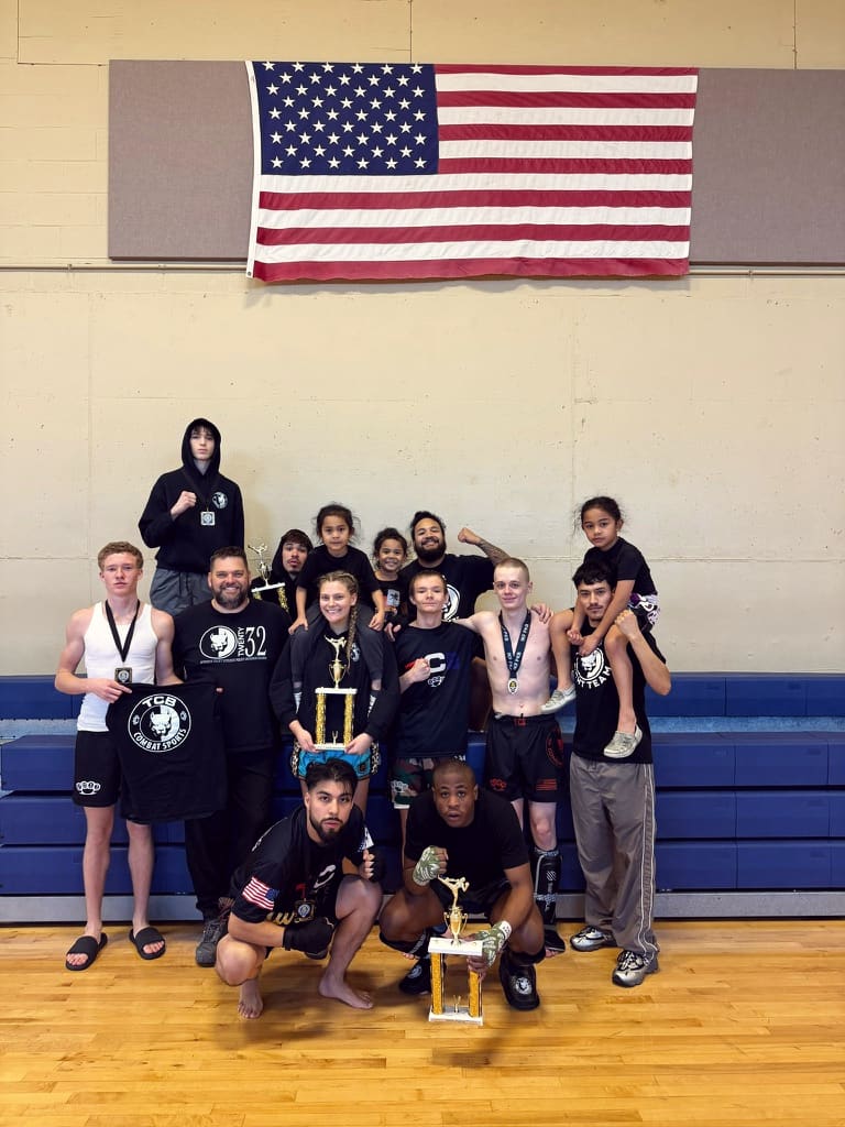TCB athletes and coaches gather under an American flag with their trophies.